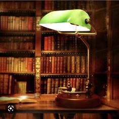 a green lamp sitting on top of a wooden table in front of a bookshelf