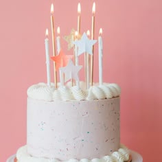 a birthday cake with white frosting and stars on top is lit up by candles