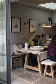 three women sitting at a table with plates and bowls on it, in a kitchen