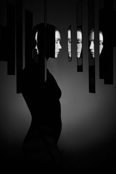 a woman standing in front of mirrors with her head turned to the side, and another person's reflection behind her