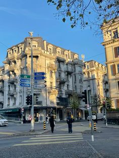 two people walking across the street in front of a building