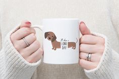 a woman holding a coffee mug with a brown dachshund dog on it