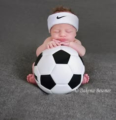 a baby laying on the ground with a soccer ball in its mouth and wearing a headband