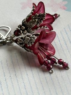 "Gorgeous burgundy wine blossoms, cloaked in ornate leafy caps, dangle hand-cut tiny garnets from velvety throats. Choice of gunmetal (photos 6,7 and 8) for those who prefer a darker goth look or antique silver (photos 1 thru 5) for a more romantic vintage look. These lovely lilies measure 1 5/8\" (41mm) from the bottom loop of the gunmetal/ antique silver kidney earwires. Prefer a different style of earwire? French earwires, leverbacks, and non-pierced clips are also available...please choose y Elegant Handmade Burgundy Jewelry, Handmade Burgundy Jewelry For Parties, Elegant Red Handmade Flower Earrings, Elegant Handmade Red Flower Earrings, Lucite Flower Earrings, Lily Earrings, Red Flower Earrings, Beaded Jewelry Earrings, Polymer Clay Flower Jewelry