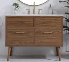 a bathroom vanity with a round mirror above it and plants in vases on the side