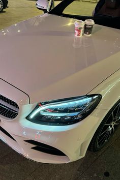 a white car parked in a parking lot next to two cups of coffee on top of it