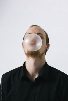 a man with a beard blowing bubbles into the air by an object in front of his face