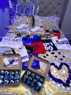 the bed is covered with blue and white items, including t - shirts and necklaces