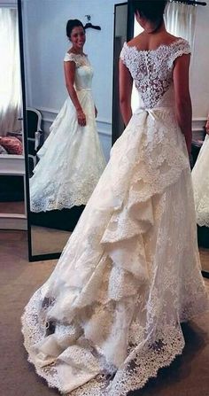 a woman standing in front of a mirror wearing a wedding dress with ruffles