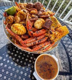 there is a bowl full of cooked crabs and corn on the cob next to a cup of sauce