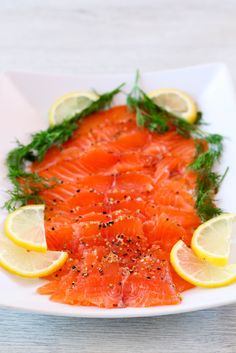 a white plate topped with sliced up salmon and lemon wedges