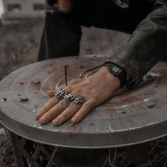 a person's hand resting on top of a metal table in the middle of grass