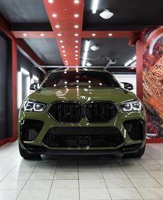 the front end of a green bmw suv in a showroom with red and white walls