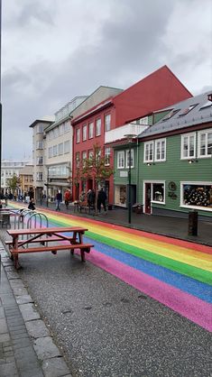 a rainbow painted bench in the middle of a street with people walking on it and buildings