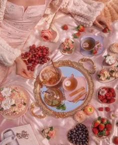 a woman sitting at a table filled with plates and bowls full of food, including strawberries