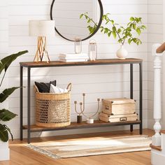 a console table with books, plants and a round mirror on the wall above it