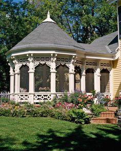 a white gazebo sitting in the middle of a lush green field next to a yellow house