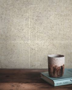 a coffee cup sitting on top of a book next to a wallpapered wall