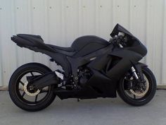 a black motorcycle is parked in front of a building with a white wall behind it