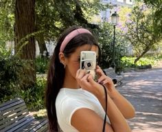 a woman taking a photo with her cell phone while sitting on a bench in the park