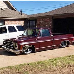 an old red truck parked in front of a white car on a driveway next to a house