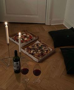 two pizzas and wine on the floor in front of a white door with candles