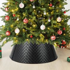 a small christmas tree in a black pot with ornaments on it and presents around the base