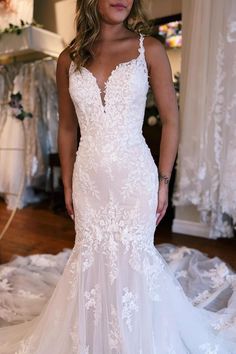 a woman wearing a white wedding dress standing in front of a bed full of clothes