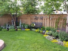 a garden with lots of flowers and plants in the grass next to a wooden fence