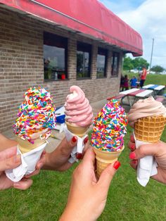 three ice cream cones with sprinkles are being held by two women in front of a building