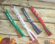 four tasseled keychains are sitting on a wooden table with autumn leaves