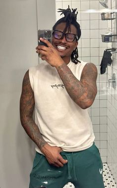 a man taking a selfie in the bathroom while wearing green shorts and a white t - shirt