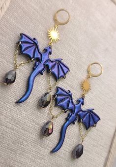 two blue dragon keychains are hanging on a white cloth with gold chains and dangling earrings