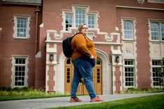 a woman is standing in front of a brick building with large windows and a backpack on her back