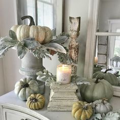 a white dresser topped with lots of different types of pumpkins and greenery next to a mirror