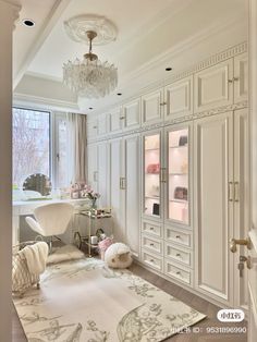 a room with white furniture and a chandelier hanging from the ceiling in front of a large window