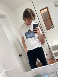 a man is taking a selfie in the mirror with his cell phone while wearing a t - shirt