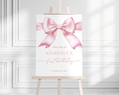 an easel with a pink bow on it and the words welcome to kimberly's first birthday