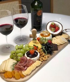 an assortment of cheeses, meats and fruit on a wooden platter with two glasses of wine