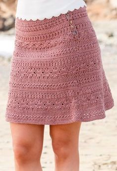 a woman wearing a pink crochet skirt and white top standing on the beach