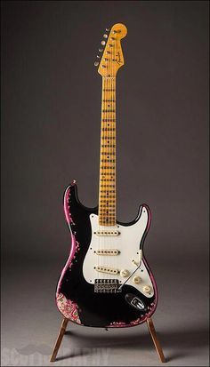 an electric guitar sitting on top of a wooden stand in front of a gray background