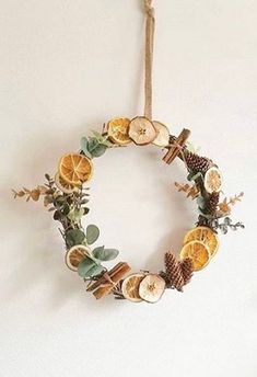 a wreath made out of oranges and pine cones hanging on a wall with greenery