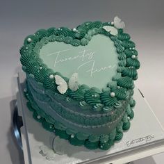 a heart - shaped cake with green frosting and white butterflies on it, sitting on top of a table