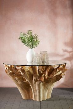 a glass table topped with a vase and a plant sitting on top of a wooden stump