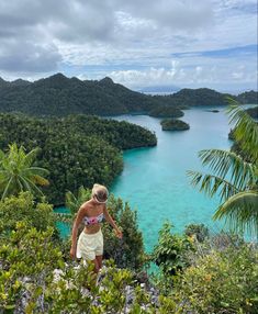 a woman standing on top of a lush green hillside next to trees and blue water