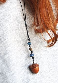 a close up of a person wearing a necklace with an acorn and beads on it