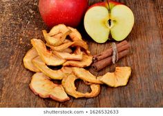 apple slices and cinnamon sticks on a wooden table with an apple in the back ground