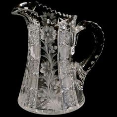 a clear glass pitcher with flowers and leaves on the bottom, sitting in front of a black background