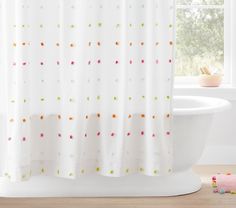 a white shower curtain with multicolored dots on it next to a bathtub