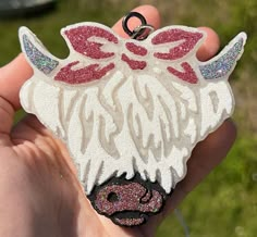 a hand holding a white and red brooch with pink glitters on it's face